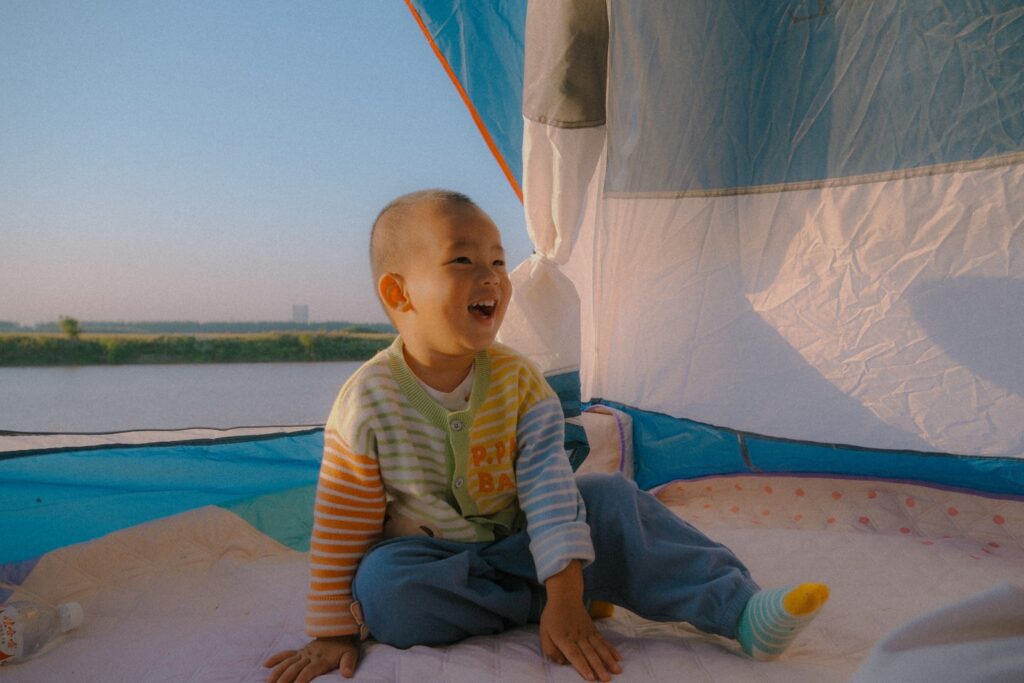 A little boy sitting on the ground in front of a sail boat