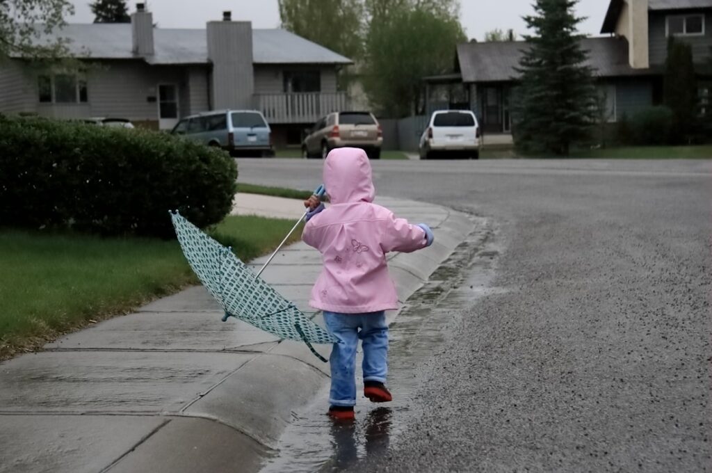 Enfant en imperméable rose marchant sous la pluie sur le trottoir, parapluie à la main