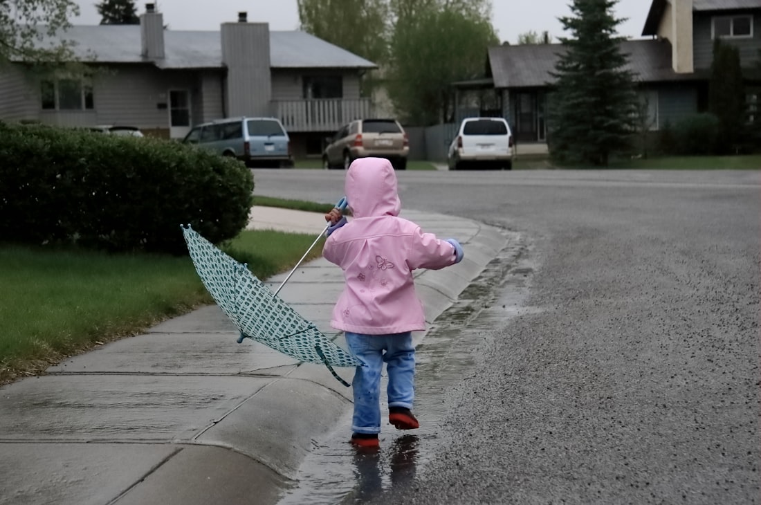 Enfant en imperméable rose marchant sous la pluie sur le trottoir, parapluie à la main