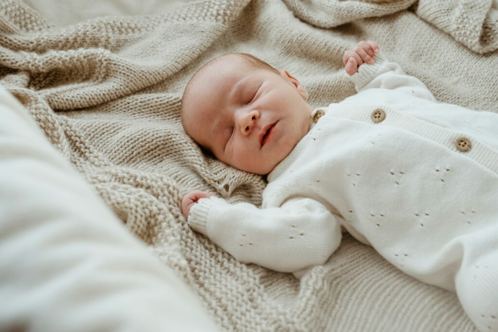 Nouveau-né endormi sur le dos, en grenouillère blanche, sur un plaid en maille beige